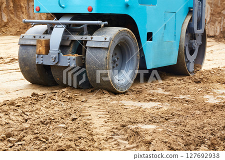 Construction site features a blue roller compacting earth on a freshly excavated ground during daylight hours 127692938