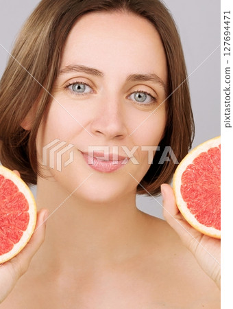 Portrait of a Caucasian woman with flawless skin holding two grapefruit halves on a grey background. Ads natural skincare, vegan cosmetics, citrus oils and detox diet for a healthy, glowing complexion Portrait of a Caucasian woman with flawless skin holding two grapefruit halves on a grey background. Ads natural skincare, vegan cosmetics, citrus oils and detox diet for a healthy, glowing complexion 127694471