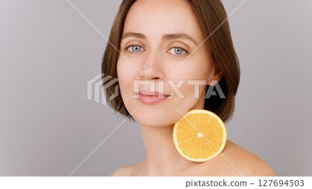 Caucasian beautiful brunette woman, face and orange in beauty skincare for vitamin C detox. Grey background. Close-up portrait of pretty female, calm model with natural organic fruit. Ads healthy skin Caucasian beautiful brunette woman, face and orange in beauty skincare for vitamin C detox. Grey background. Close-up portrait of pretty female, calm model with natural organic fruit. Ads healthy skin 127694503