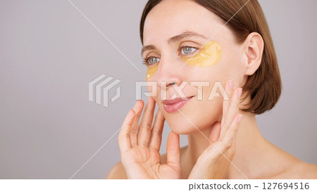 Eye patch ads concept. Aesthetic woman applying under-eye recovery patches. Charming calm brunette woman in studio on grey background. Cosmetics Beauty routine Dermatology Rejuvenation Spa Skincare Eye patch ads concept. Aesthetic woman applying under-eye recovery patches. Charming calm brunette woman in studio on grey background. Cosmetics Beauty routine Dermatology Rejuvenation Spa Skincare 127694516