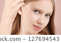 Skincare. Close-up portrait of a young Caucasian girl applying facial serum with a dropper. Pink background. Concept beauty ads, wellness blogs, cosmetic product promotions for teenagers, smooth skin 127694543