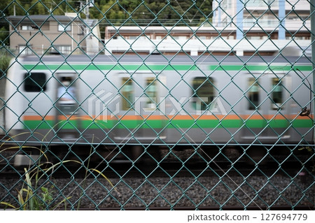 Tokaido Line: A passing train and conductor captured through the wire mesh of a pedestrian bridge 127694779