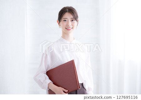 A woman in a pink sheer shirt holding a file on a white background, looking at the camera. Real estate job changes, professional services, human resources, etc. A woman in a pink sheer shirt holding a file on a white background, looking at the camera. Real estate job changes, professional services, human resources, etc. 127695116
