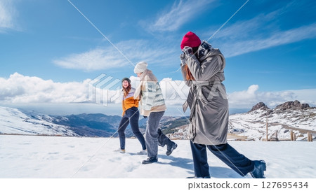 Three tourists walking on snowy mountain top enjoying winter landscape 127695434