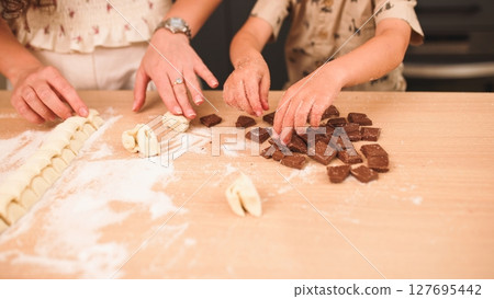 Mother and child preparing chocolate filled pastries on kitchen table 127695442