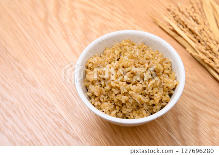 Brown rice and ears of rice in a bowl on a wooden table background Brown rice and ears of rice in a bowl on a wooden table background 127696280