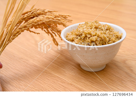 Brown rice and ears of rice in a bowl on a wooden table background 127696434