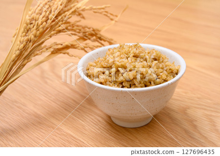 Brown rice and ears of rice in a bowl on a wooden table background 127696435
