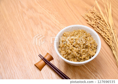 Brown rice and ears of rice in a bowl on a wooden table background Brown rice and ears of rice in a bowl on a wooden table background 127696535