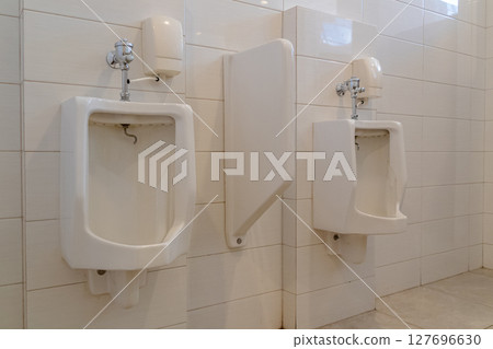 White ceramic urinal with flush valve mounted on tiled wall in public restroom White ceramic urinal with flush valve mounted on tiled wall in public restroom 127696630