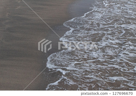 Close-up view of textured white ocean foam meeting dark brown sand 127696670