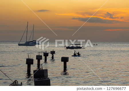 Tranquil ocean scene at dusk showing anchored boats and concrete pillars in water 127696677