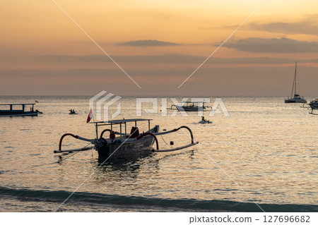 Traditional Indonesian outrigger boats float peacefully on the golden ocean at sunset 127696682