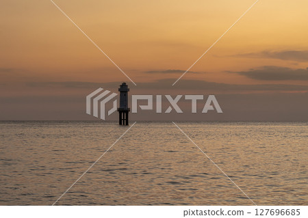 Peaceful coastal landscape with a distant lighthouse against a colorful evening glow Peaceful coastal landscape with a distant lighthouse against a colorful evening glow 127696685