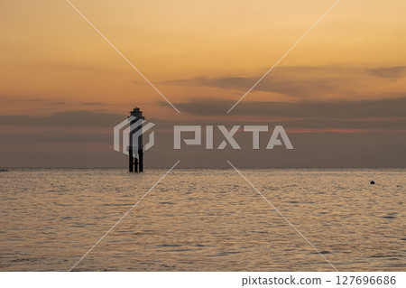 Peaceful coastal landscape with a distant lighthouse against a colorful evening glow 127696686