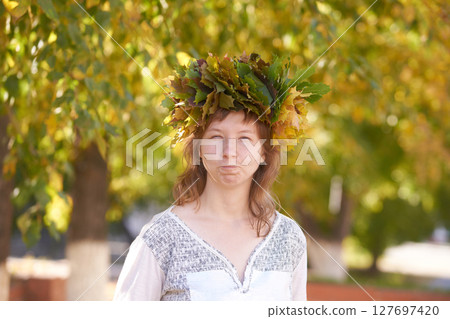 Young caucasian female with leaf crown expressing joy amidst autumn trees 127697420