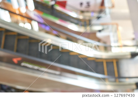 Blurry view of escalators in shopping mall with colorful lights and reflections 127697430