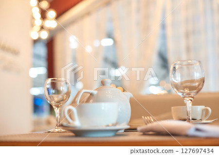 Elegant table setting with white teapot and glassware in cozy cafe ambiance Elegant table setting with white teapot and glassware in cozy cafe ambiance 127697434