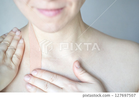 Female adult caucasian applying therapeutic kinesiology tape to shoulder neck 127697507