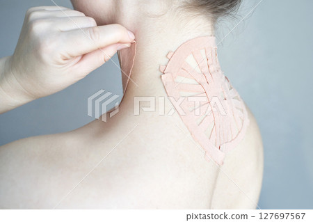 Female applying therapeutic tape on upper back for pain relief and posture  127697567