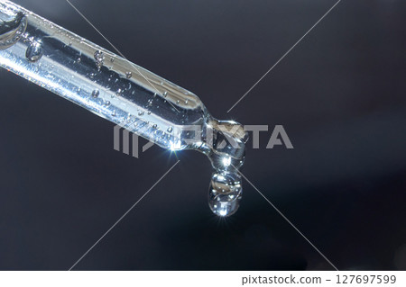 Close-up of transparent glass dropper with droplet against dark background 127697599