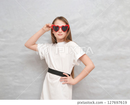 Young caucasian girl posing in heart-shaped sunglasses and white t-shirt against 127697619