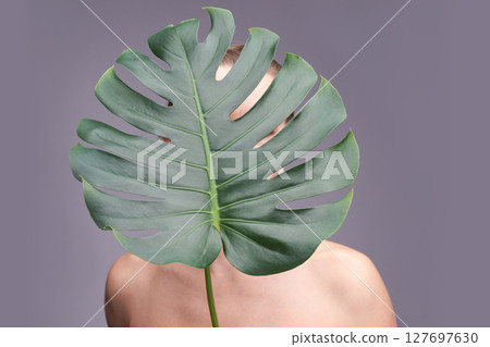 Female with monstera leaf covering face on gray background showcasing natural Female with monstera leaf covering face on gray background showcasing natural 127697630