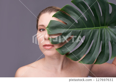 Caucasian adult female with monstera leaf against gray background in artistic Caucasian adult female with monstera leaf against gray background in artistic 127697631