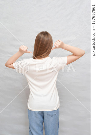 Young caucasian female in white t-shirt and jeans posing with thumbs pointing Young caucasian female in white t-shirt and jeans posing with thumbs pointing 127697661