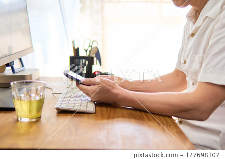 一位 50 多歲的男子在電腦工作間隙查看手機 127698107