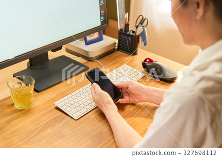 A man in his 50s checking his cell phone between computer work 127698112