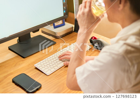 A man in his 50s drinking a glass of tea while typing on a keyboard A man in his 50s drinking a glass of tea while typing on a keyboard 127698123