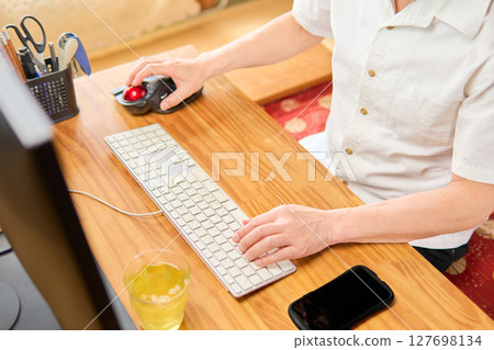 A man in his 50s typing on a keyboard while operating a mouse at a computer 127698134