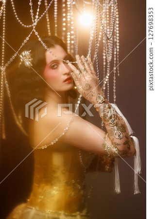 Retro-style performer in vintage costume posing on dark stage under chandelier 127698353