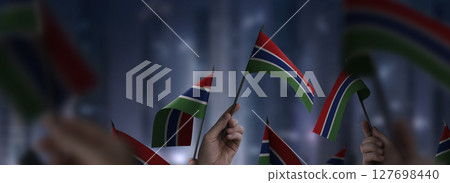 Gambia flags in their hands on a blurred urban background Gambia flags in their hands on a blurred urban background 127698440