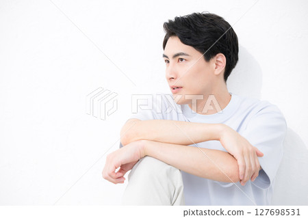 Handsome man with a serious expression sitting and leaning against a wall Handsome man with a serious expression sitting and leaning against a wall 127698531