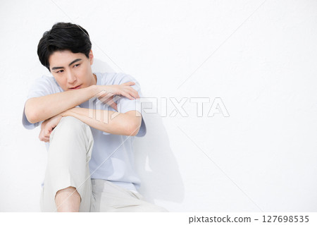 Full body of a handsome man with a serious expression sitting and leaning against a wall 127698535