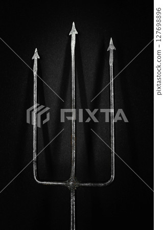 Old, rusty and metal trident casting the shadow on black background surface 127698896