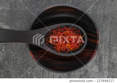 Saffron spices in black wooden spoon and bowl on black stone background 127699117