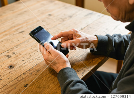 一位老人在桌邊操作智慧型手機 127699314
