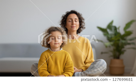 Mother and daughter in matching yellow sweaters practicing mindfulness meditation together at home Mother and daughter in matching yellow sweaters practicing mindfulness meditation together at home 127699681