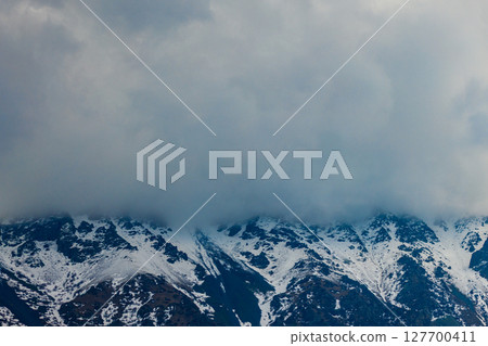 Dramatic snow-covered mountains partially obscured by clouds 127700411