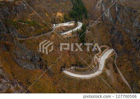 Sharp hairpin turns of road intricately carved into rugged mountainside around Voringsfossen waterfall. Starkness of natural environment in Norway Sharp hairpin turns of road intricately carved into rugged mountainside around Voringsfossen waterfall. Starkness of natural environment in Norway 127700506