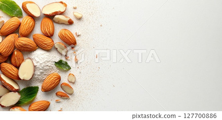 Freshly harvested almonds arranged beautifully on a clean surface with a few leaves and almond flour scattered around, showcasing their natural appeal and texture 127700886