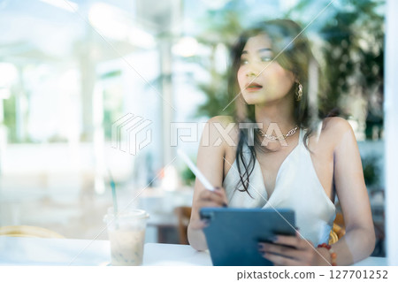 beautiful asian freelance Success people business woman fashion model in summer white sleeveless dress using casual working with tablet for browsing internet, chatting and blogging in coffee shop. 127701252