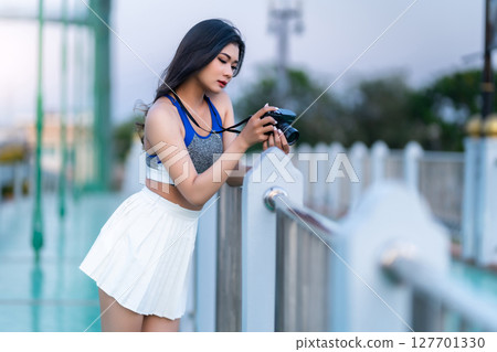 Portrait of beautiful athletic young asian woman in fashionable sportswear standing and with a holding the camera on Route walking jogging or ride bicycle and exercise on the bridge. 127701330
