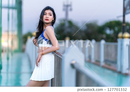 Portrait of beautiful athletic young asian woman in fashionable sportswear standing and having rest after exercise training on Route walking jogging or ride bicycle and exercise on the bridge. 127701332