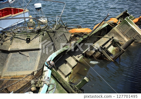 A capsized ship anchored in a harbor 127701495