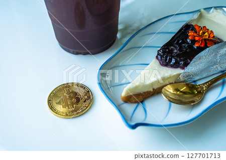 Close-up of Golden bitcoins or cryptocurrency coin or symbols and Americano iced coffee or black and Blueberry Cake in white table. Future currency concept. Close-up of Golden bitcoins or cryptocurrency coin or symbols and Americano iced coffee or black and Blueberry Cake in white table. Future currency concept. 127701713