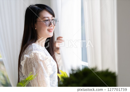 Portrait of Happy Attractive asian people cute woman wearing white lace shirt with the curtains on the window in the room felt like relaxing in house like the background 127701739